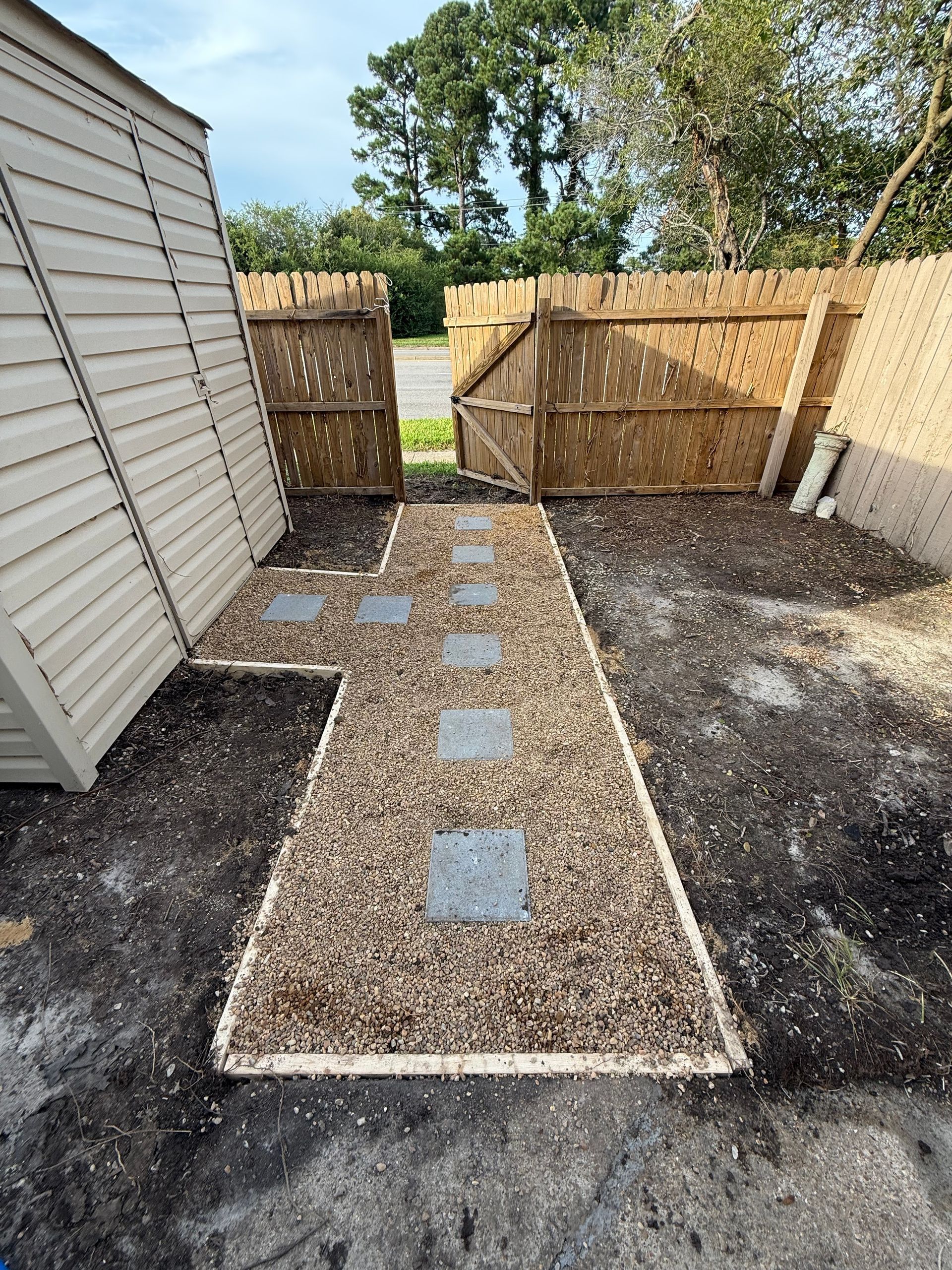 Gravel path with stepping stones between white siding and wooden fence leading to a backyard gate