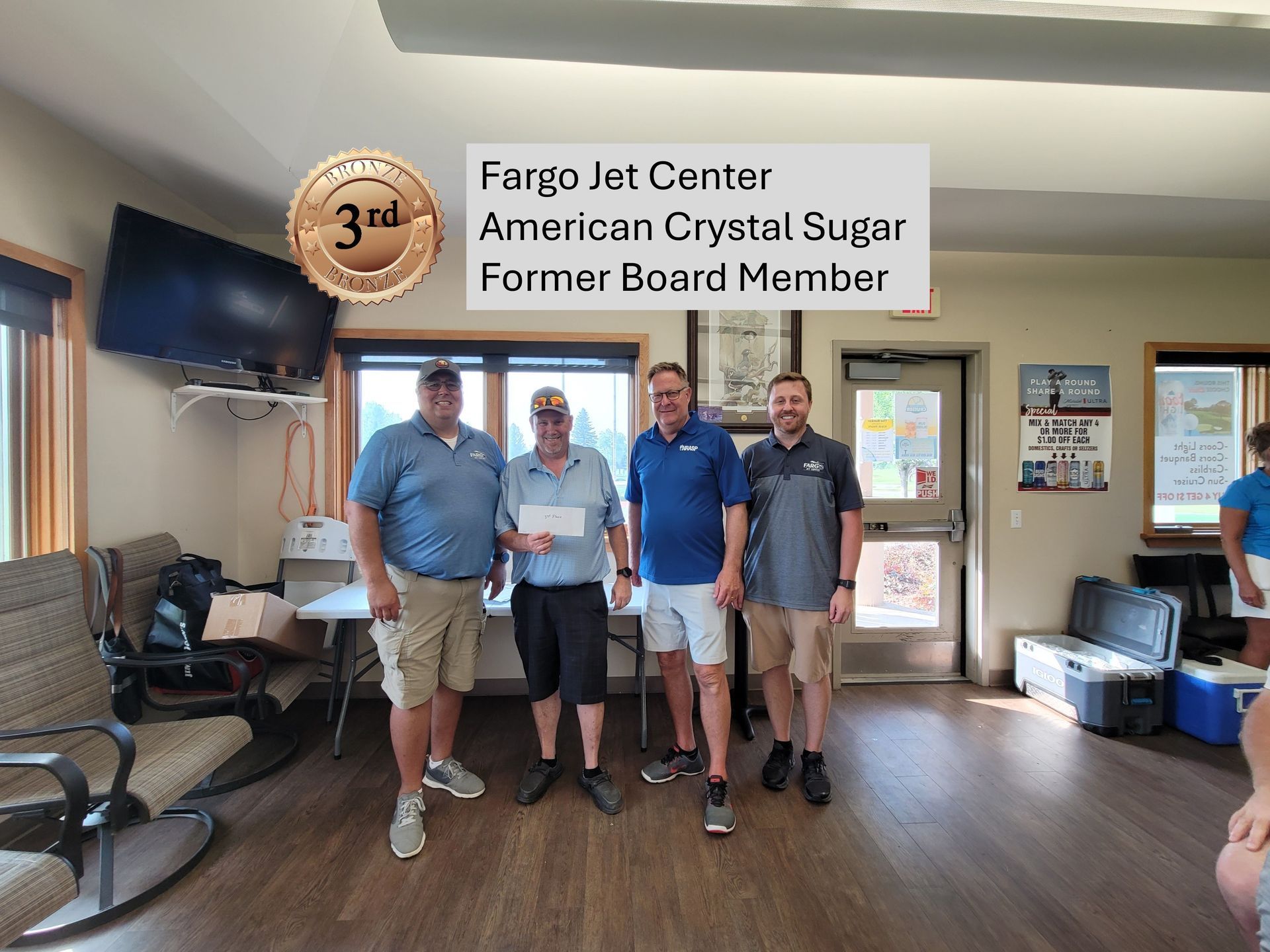 Four men holding a check, indoor room, text overlay indicates 3rd place,