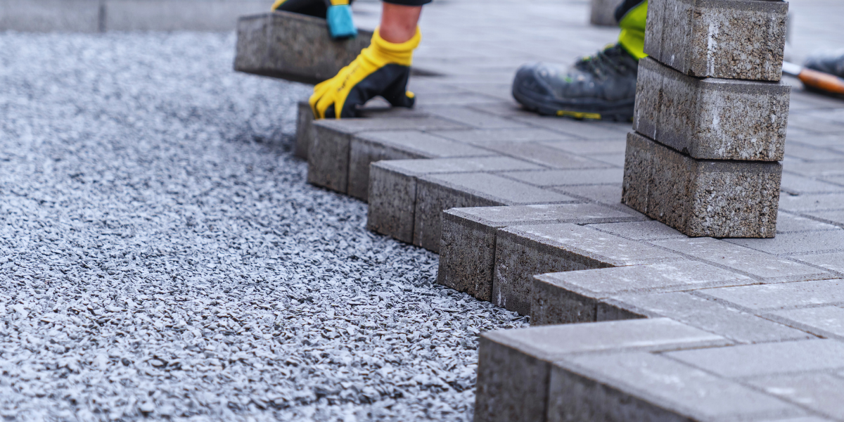 A person wearing yellow gloves is laying bricks on a sidewalk.