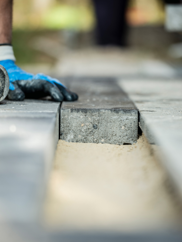 Border paver being installed A person wearing blue gloves is laying bricks on a sidewalk.