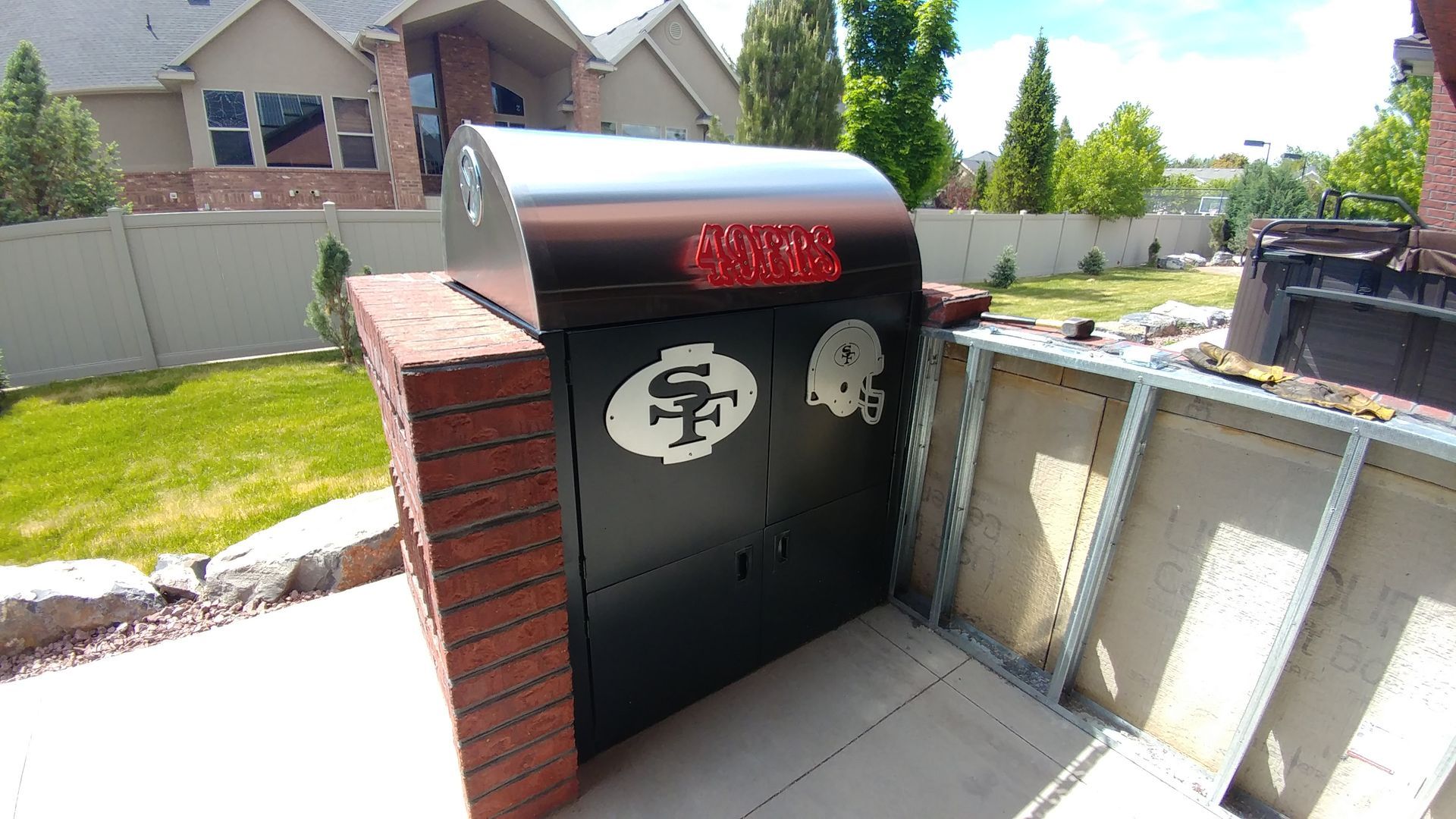 A brick and metal outdoor grill with team logos.