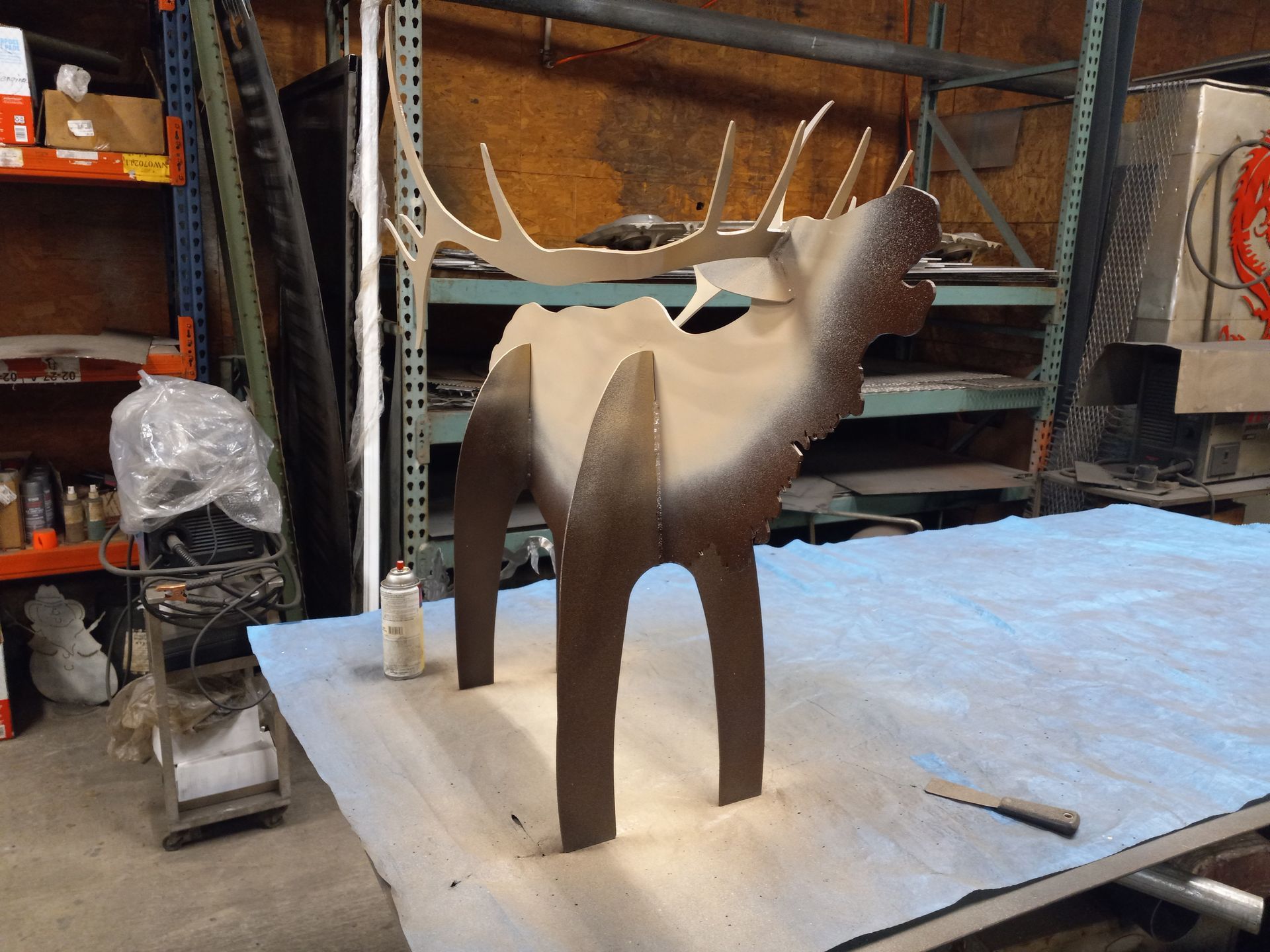 Metal elk sculpture being painted in a workshop setting.