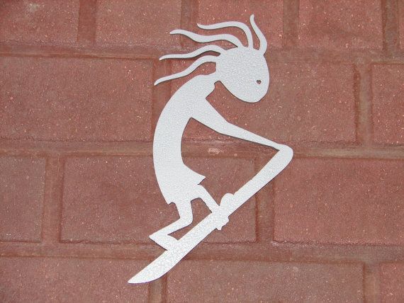 White Kokopelli figure surfing on a board against a red brick background.