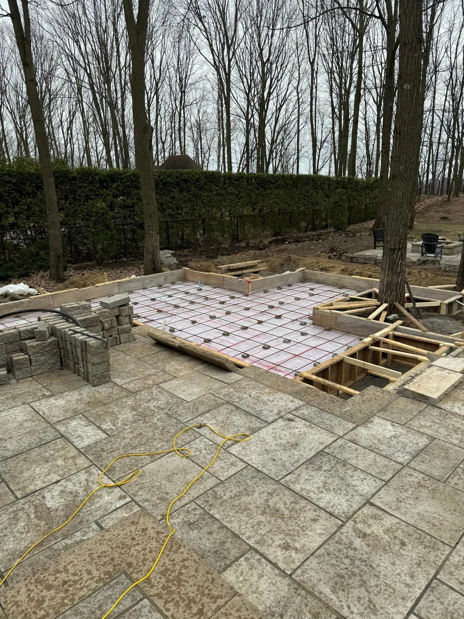 Chantier de construction avec dalles de pierre et structure partiellement construite, entouré d'arbres.