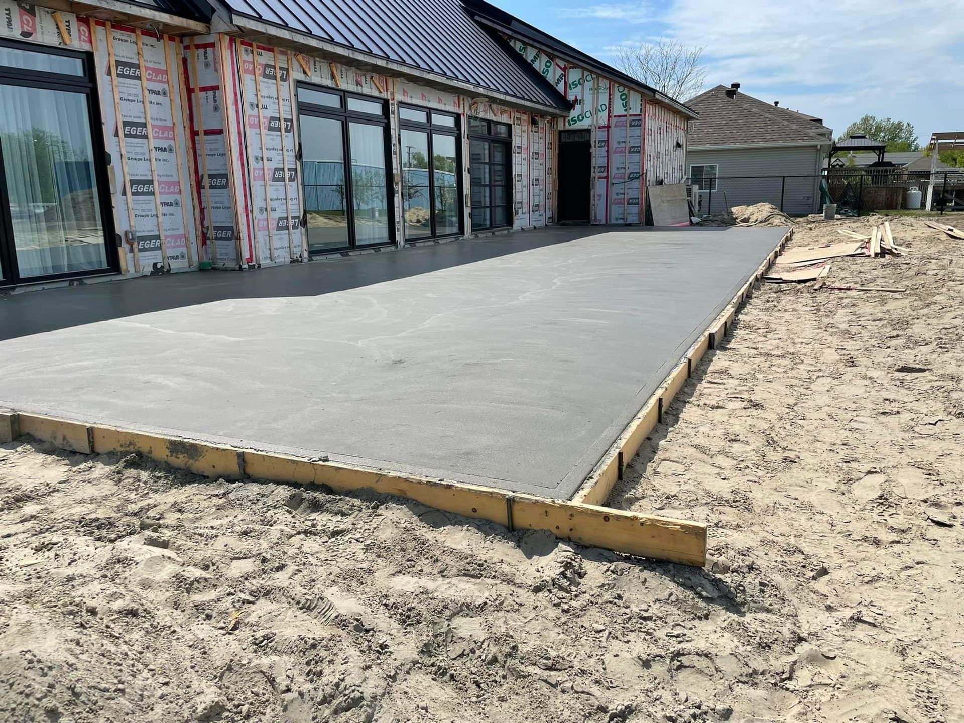 Terrasse en béton fraîchement coulée à côté d'une maison en construction.