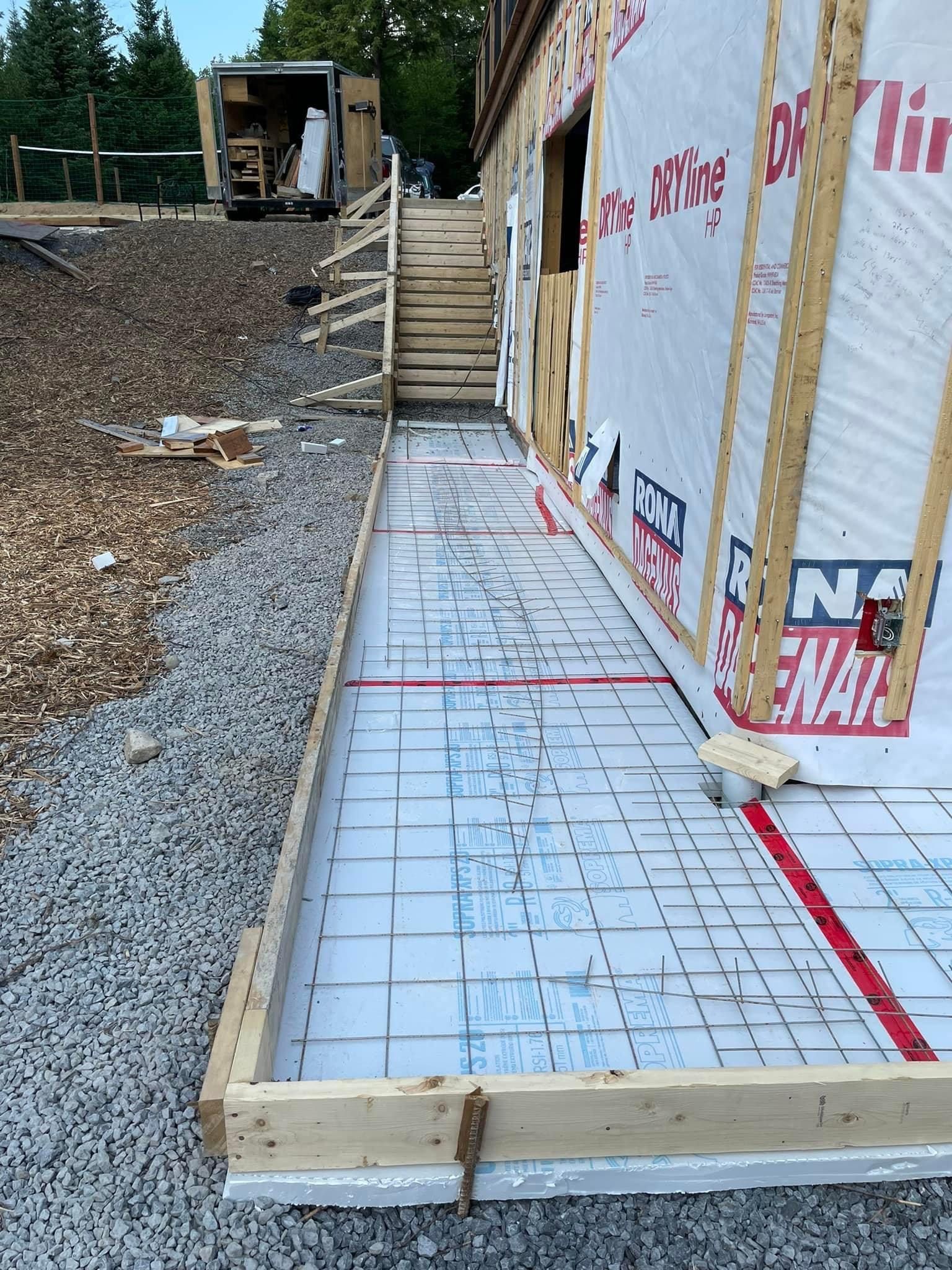 Chantier de construction avec un coffrage en bois pour un trottoir en béton. Les armatures et l'isolant sont visibles.