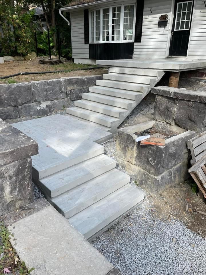 Des marches et une allée en béton gris mènent à une maison avec une porte noire et un bardage blanc.