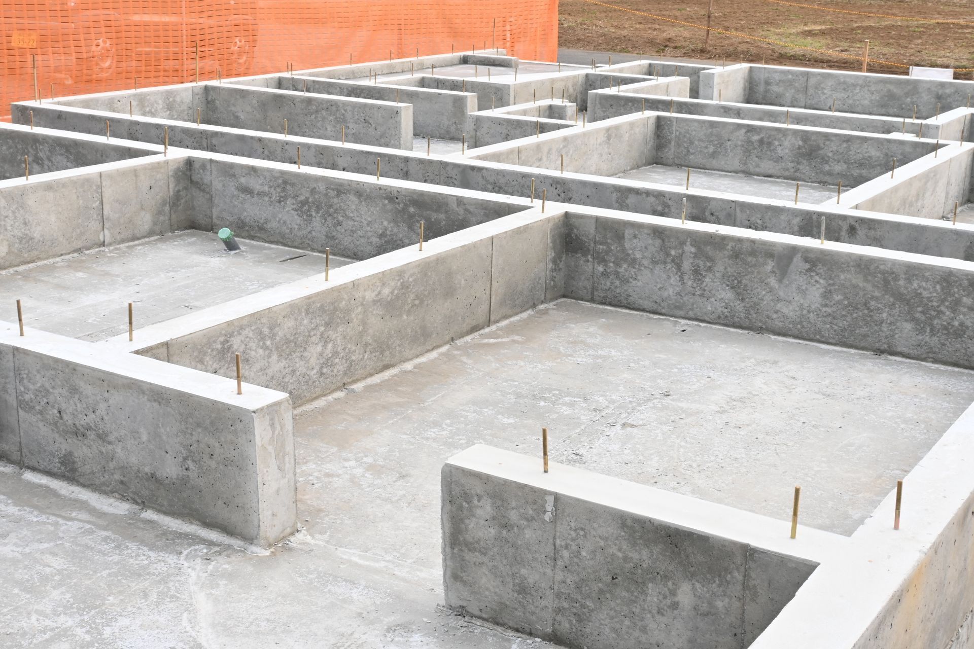 Murs de fondation en béton d'un bâtiment en construction, avec des barres d'armature apparentes, à l'extérieur.
