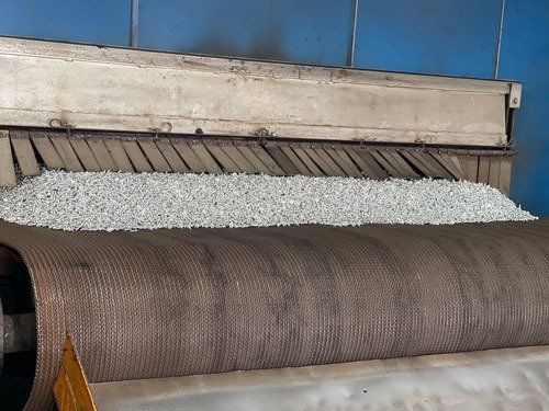 Industrial machine processing woven material in a factory, with white and brown fabric rolls.