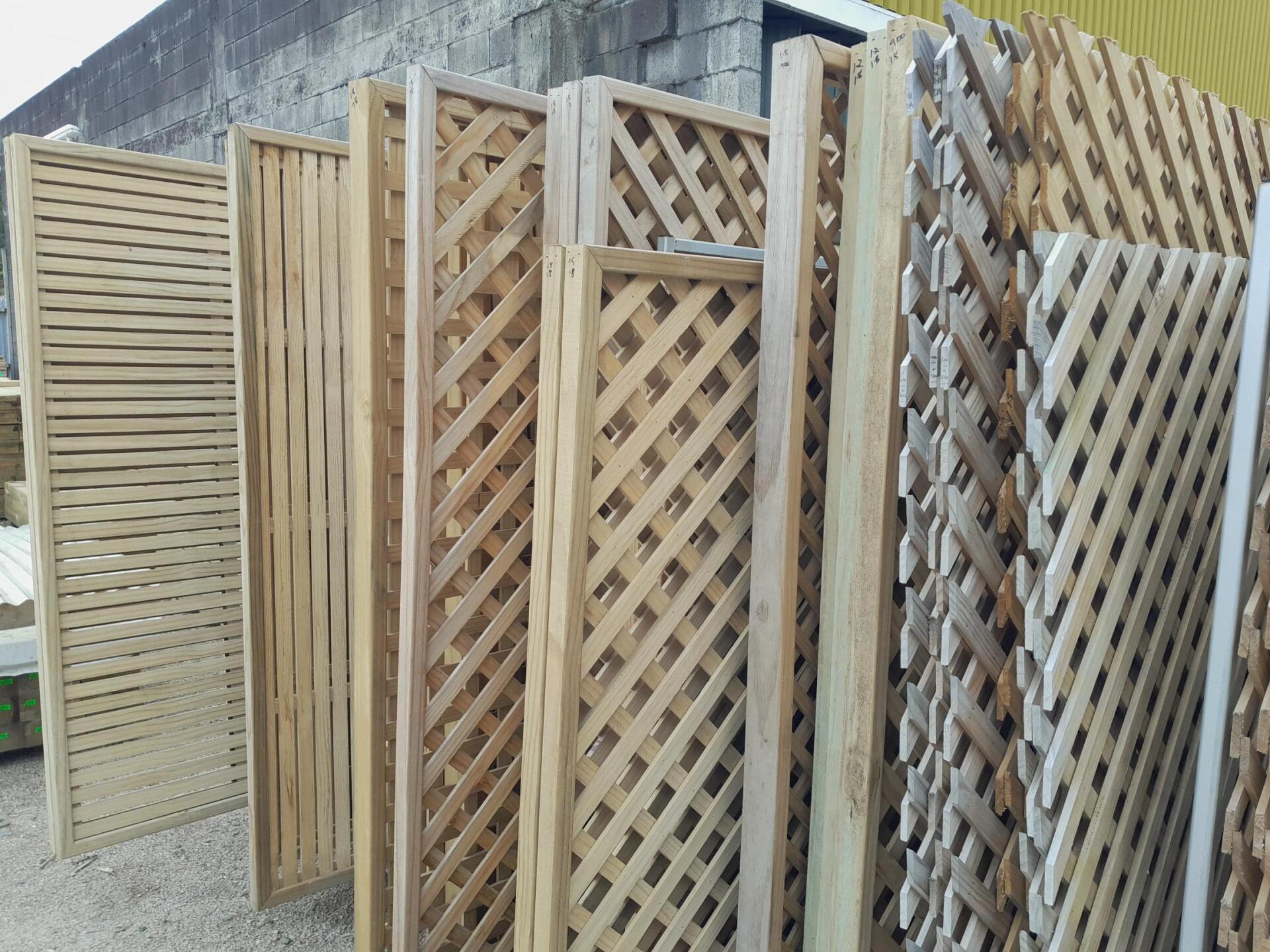 Several wooden lattice panels in varying designs stood upright in an outdoor storage area.