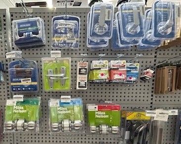 A display of various door handles and hardware products packaged in plastic containers, hanging on a retail pegboard.