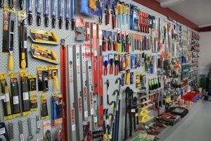A hardware store wall display featuring various hand tools like saws, files, levels, and pliers hanging on pegboards.