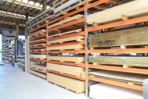 Industrial warehouse shelves stacked with rows of various wooden boards and construction plywood.