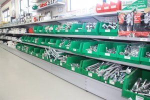 Rows of green storage bins filled with various metal hardware and fasteners on shelving in a retail hardware store.