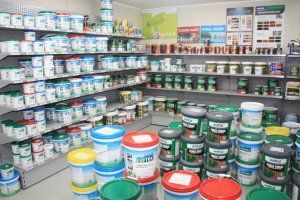 Shelves stocked with various paint cans in a retail store, with stacks of larger buckets displayed on the floor.