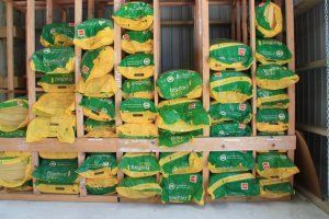 Wooden shelving unit filled with stacks of green and yellow bags of charcoal in a storage area.