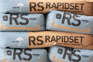 A stack of six light blue and brown paper bags of Rapidset post hole concrete, arranged in three rows of two.