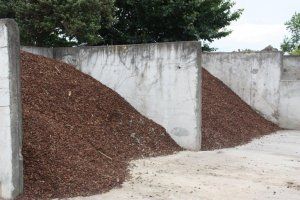 Large piles of brown mulch are stored in separate bays divided by concrete walls.