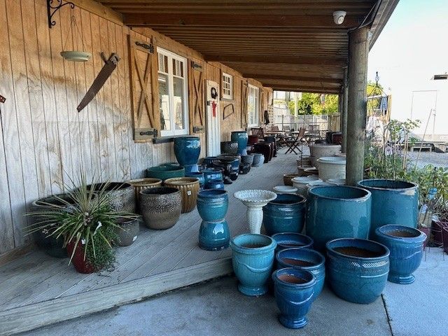 A wooden porch displaying various blue glazed and earth-toned ceramic planters, pots, and a pedestal birdbath.