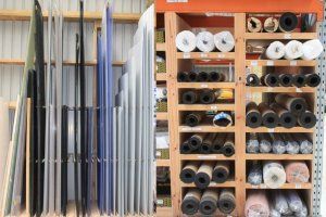 A hardware store shelf featuring vertical plastic sheets on the left and various rolls of material stored on the right.