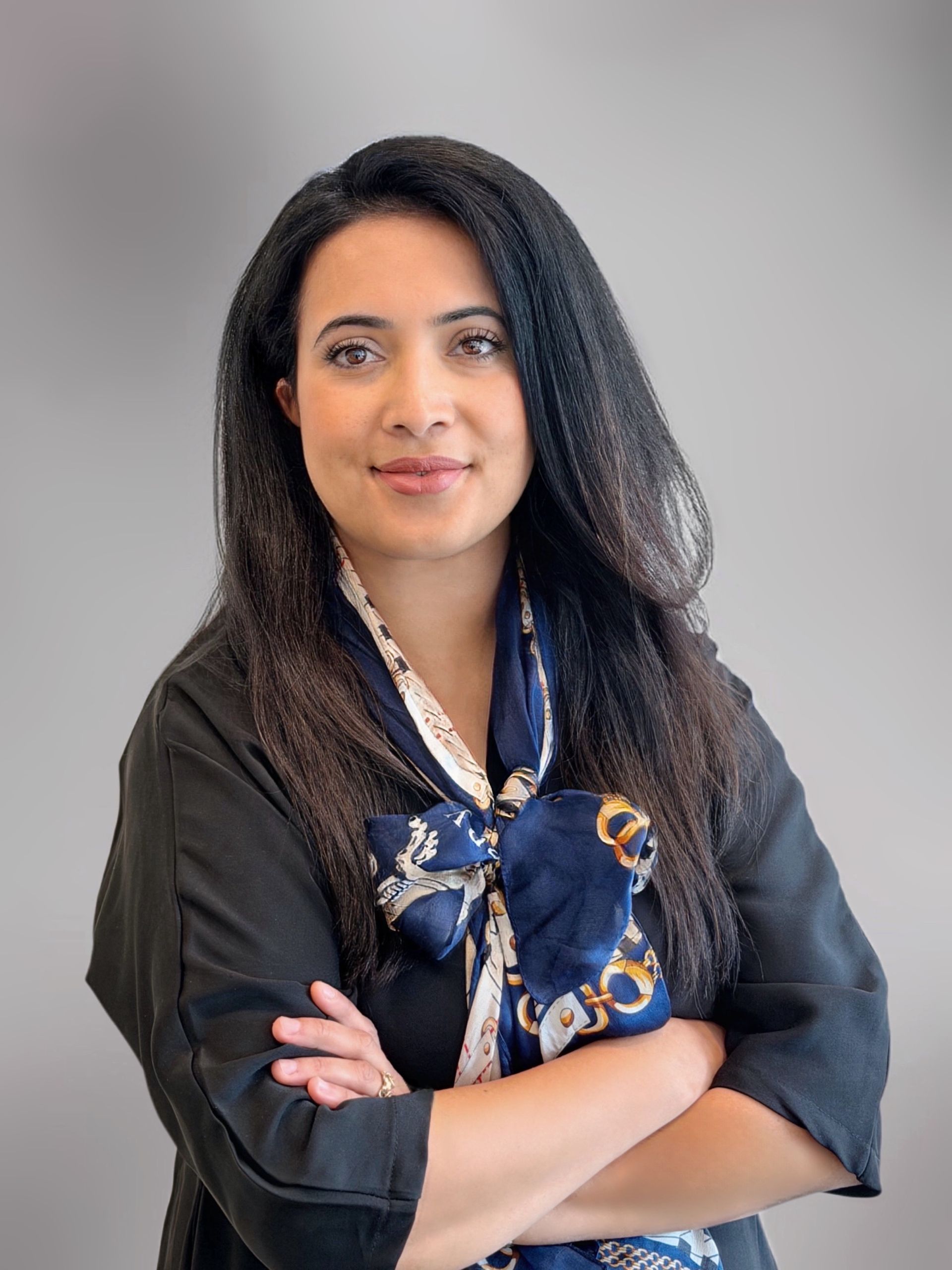 Portret van een vrouw met lang donker haar, gekleed in een lichtgekleurde blazer, tegen een witte achtergrond.