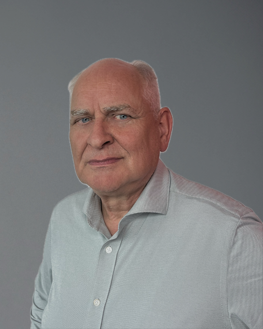 Portret van een kale man in een licht gestreept shirt tegen een grijze achtergrond.