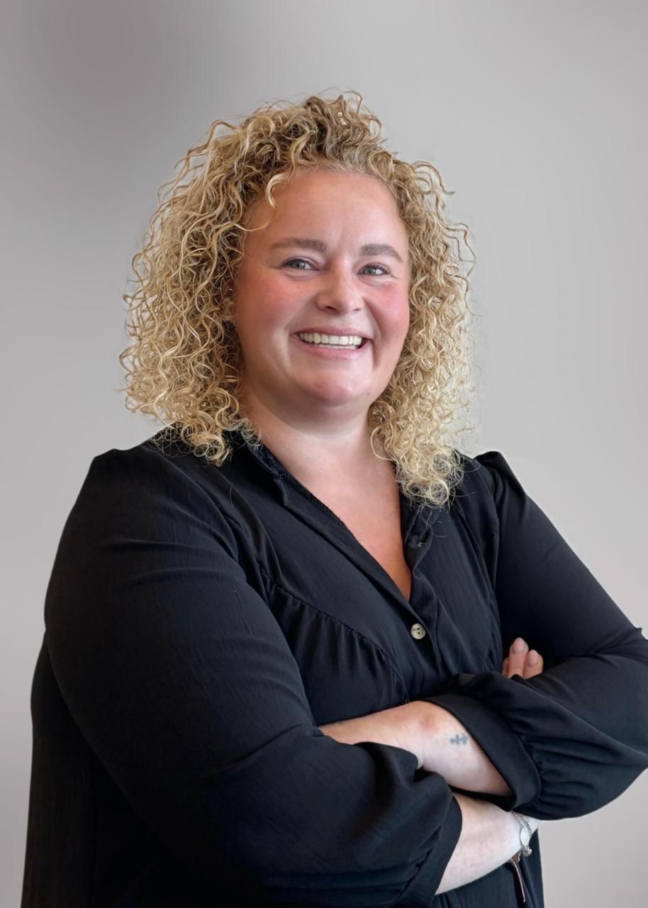 Portret van een vrouw met lang donker haar, gekleed in een lichtgekleurde blazer, tegen een witte achtergrond.