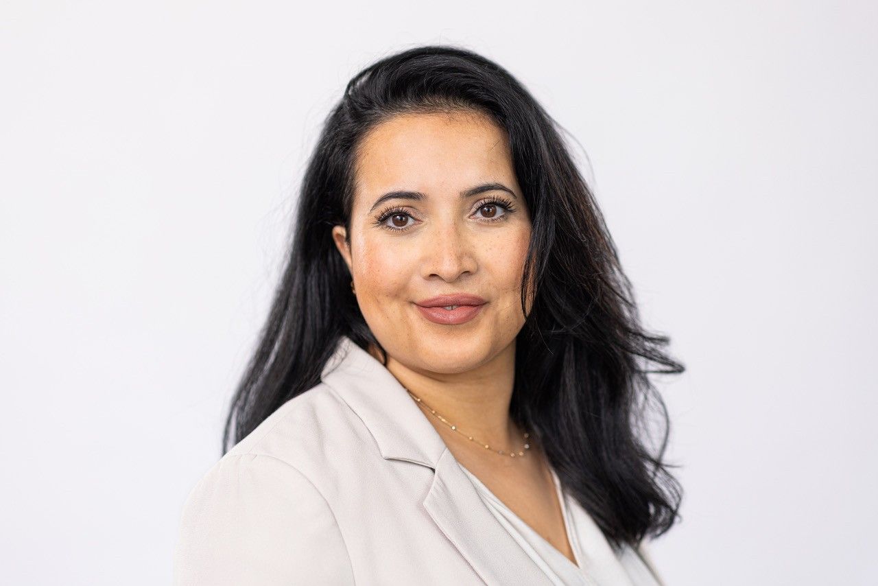 Portret van een vrouw met lang donker haar, gekleed in een lichtgekleurde blazer, tegen een witte achtergrond.