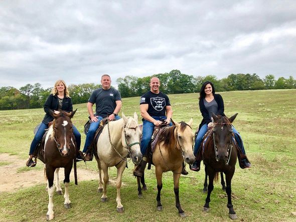 Four people riding horses in a grassy field under a cloudy sky