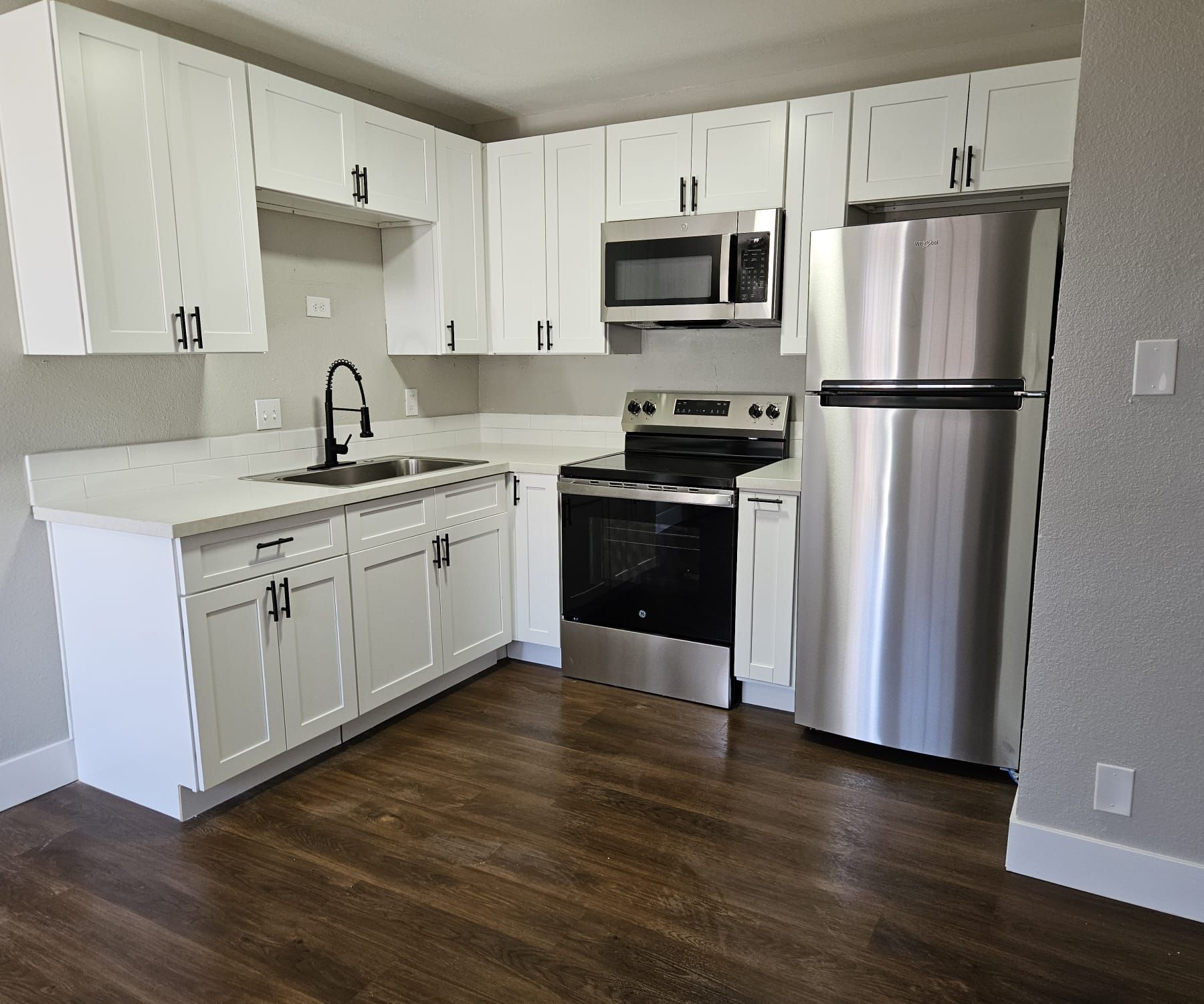 White modern kitchen with stainless steel appliances, dark wood floor, and L-shaped countertop