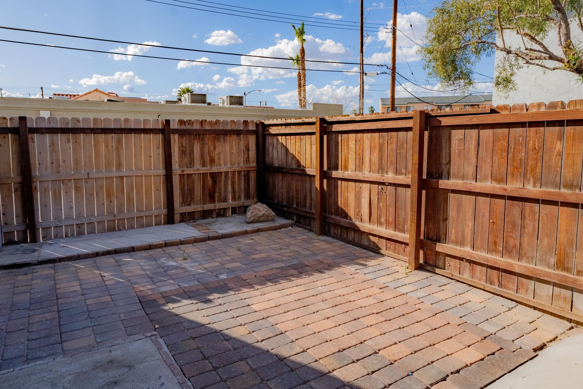Empty brick patio with wooden privacy fences and a blue sky with clouds.