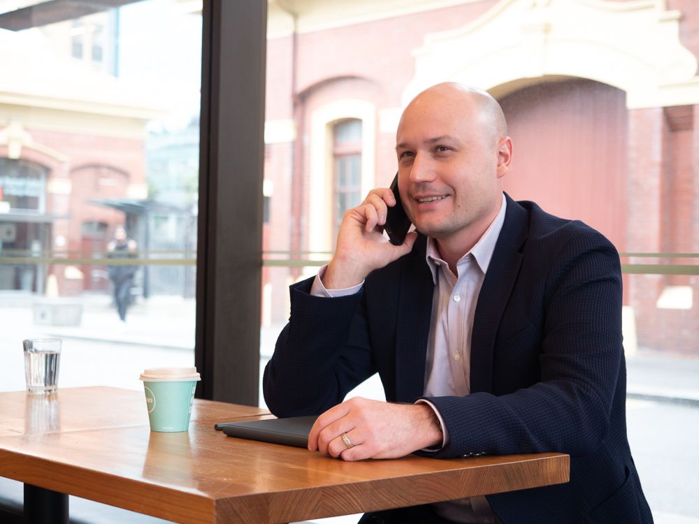 A man in a suit is sitting at a table talking on a cell phone.