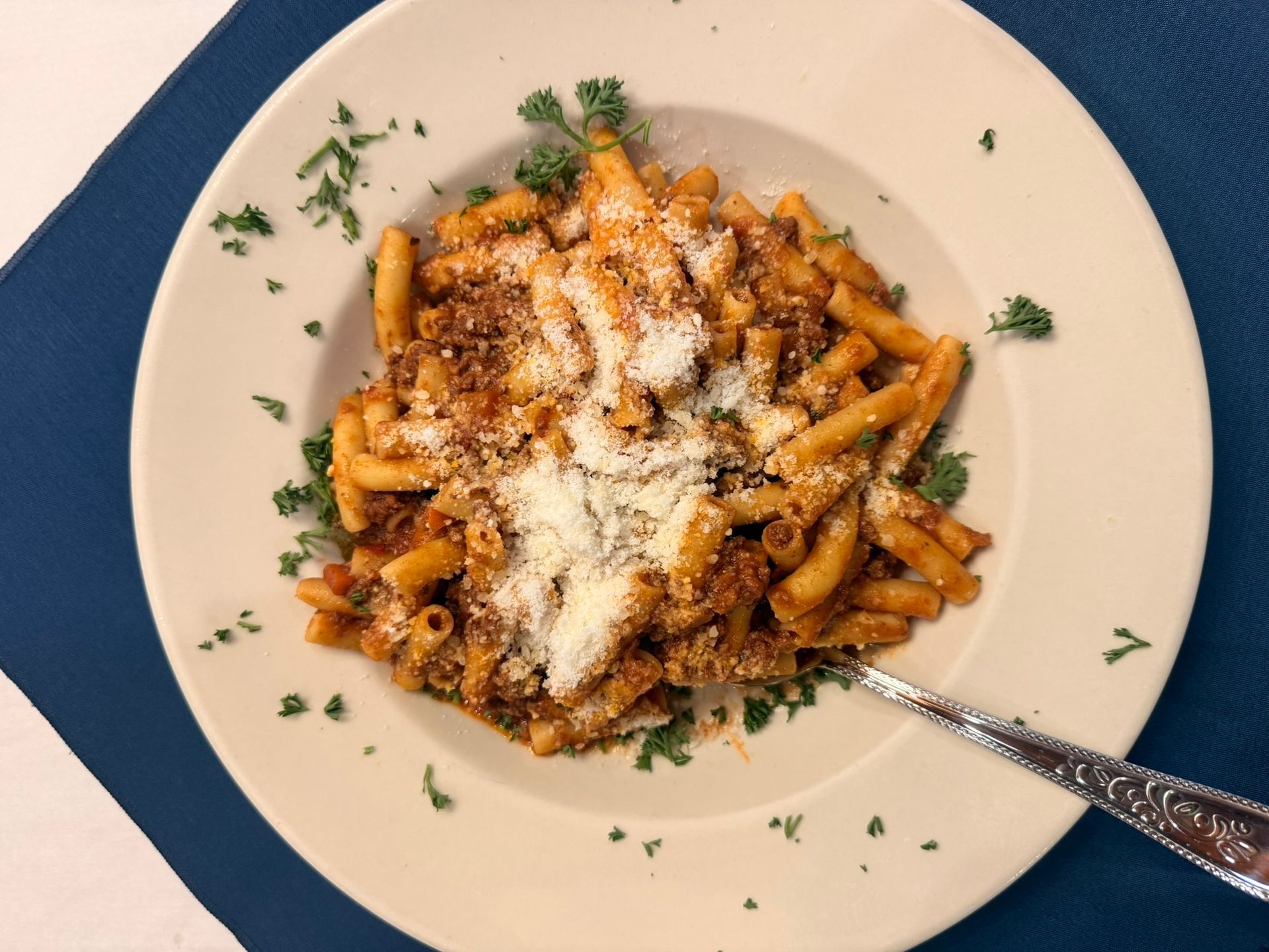 Pasta with meat sauce, topped with grated cheese and parsley, in a white bowl.