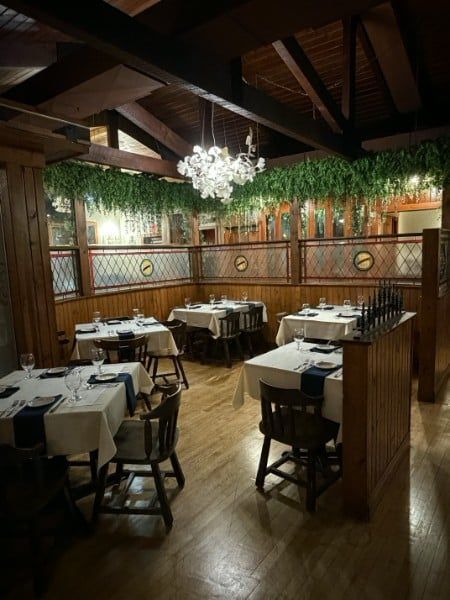 Restaurant interior with tables set for dining, wooden beams, and hanging greenery.