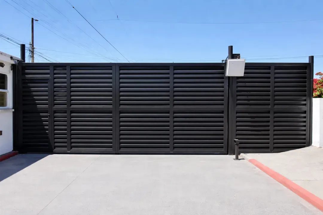 Portón corredizo de metal negro que cierra la entrada de un camino de acceso bajo un cielo azul despejado