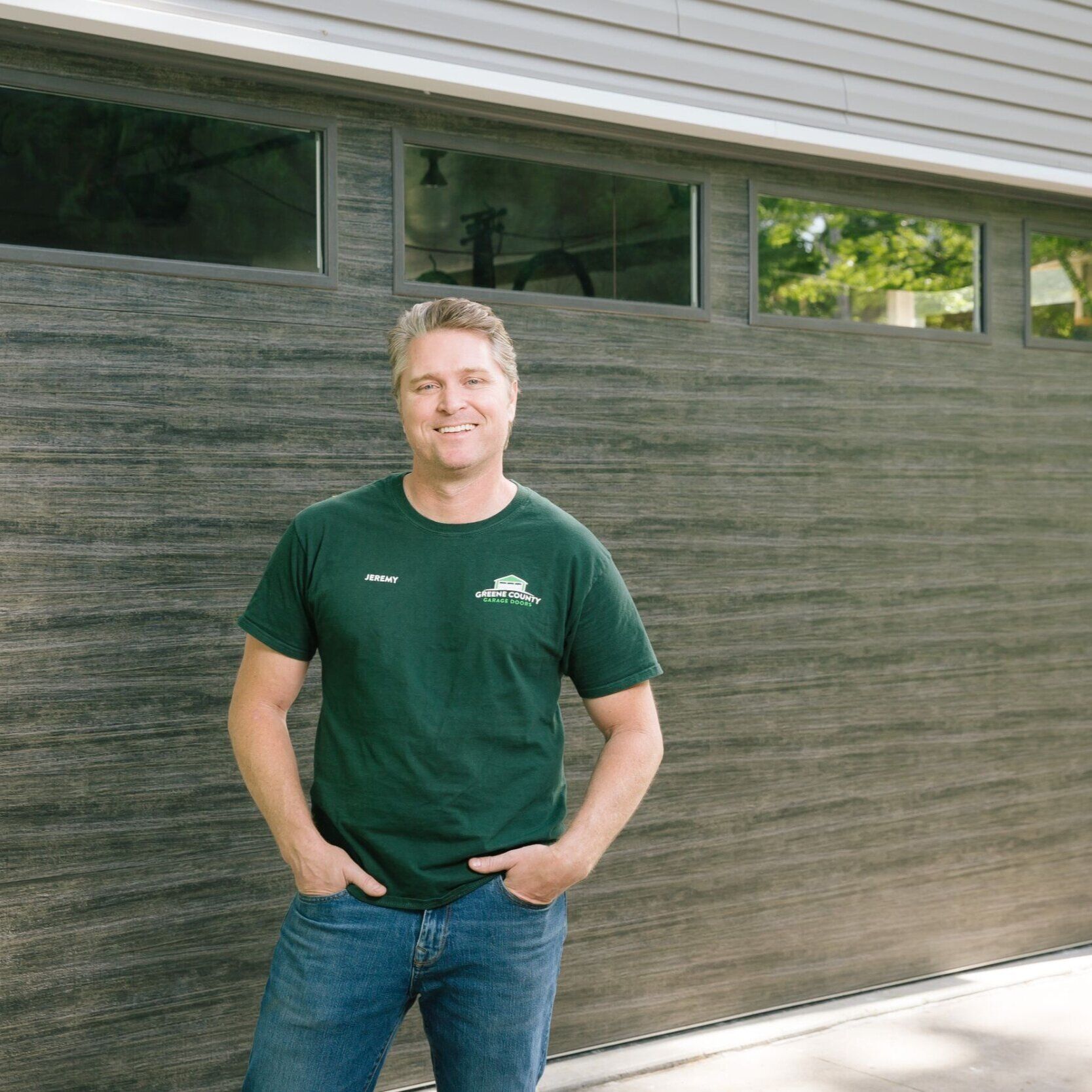 A man in a green shirt is standing in front of a garage door.