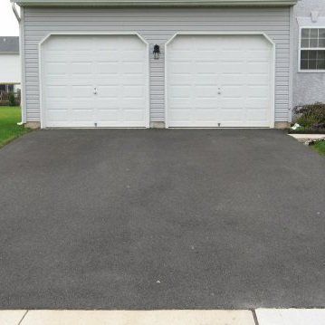 A garage with two white garage doors and a black driveway
