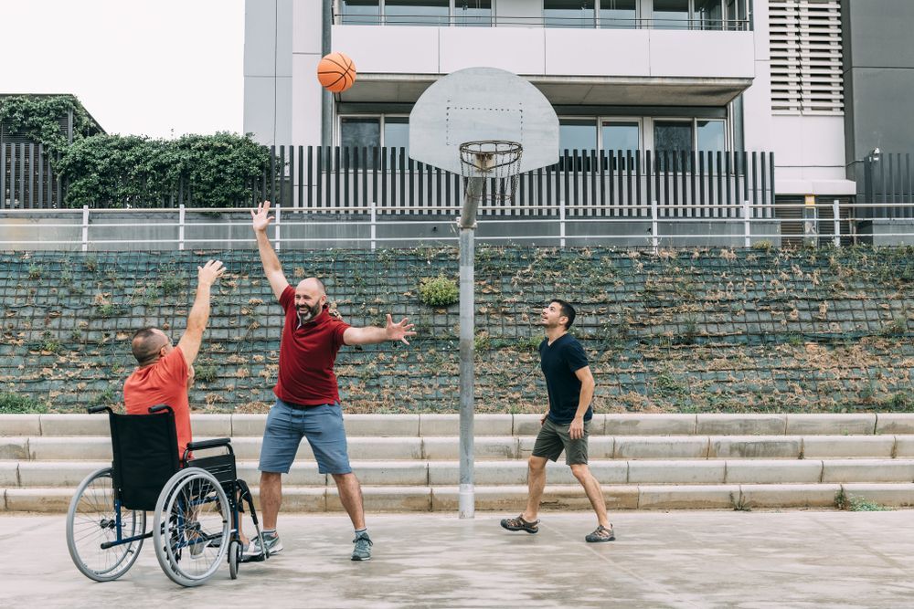 A Man in a Wheelchair is Playing Basketball With Two Other Men — Better Access Support Services In Dalby, QLD
