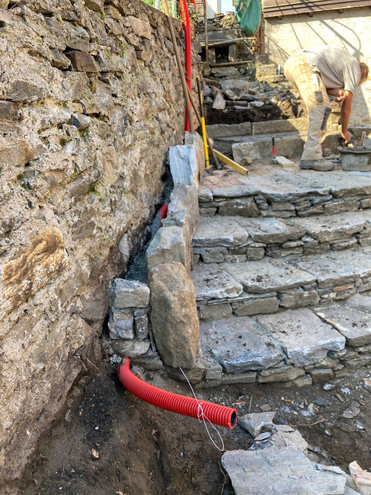 Un tubo rosso è collegato ad un muro di pietra accanto ad una rampa di scale.