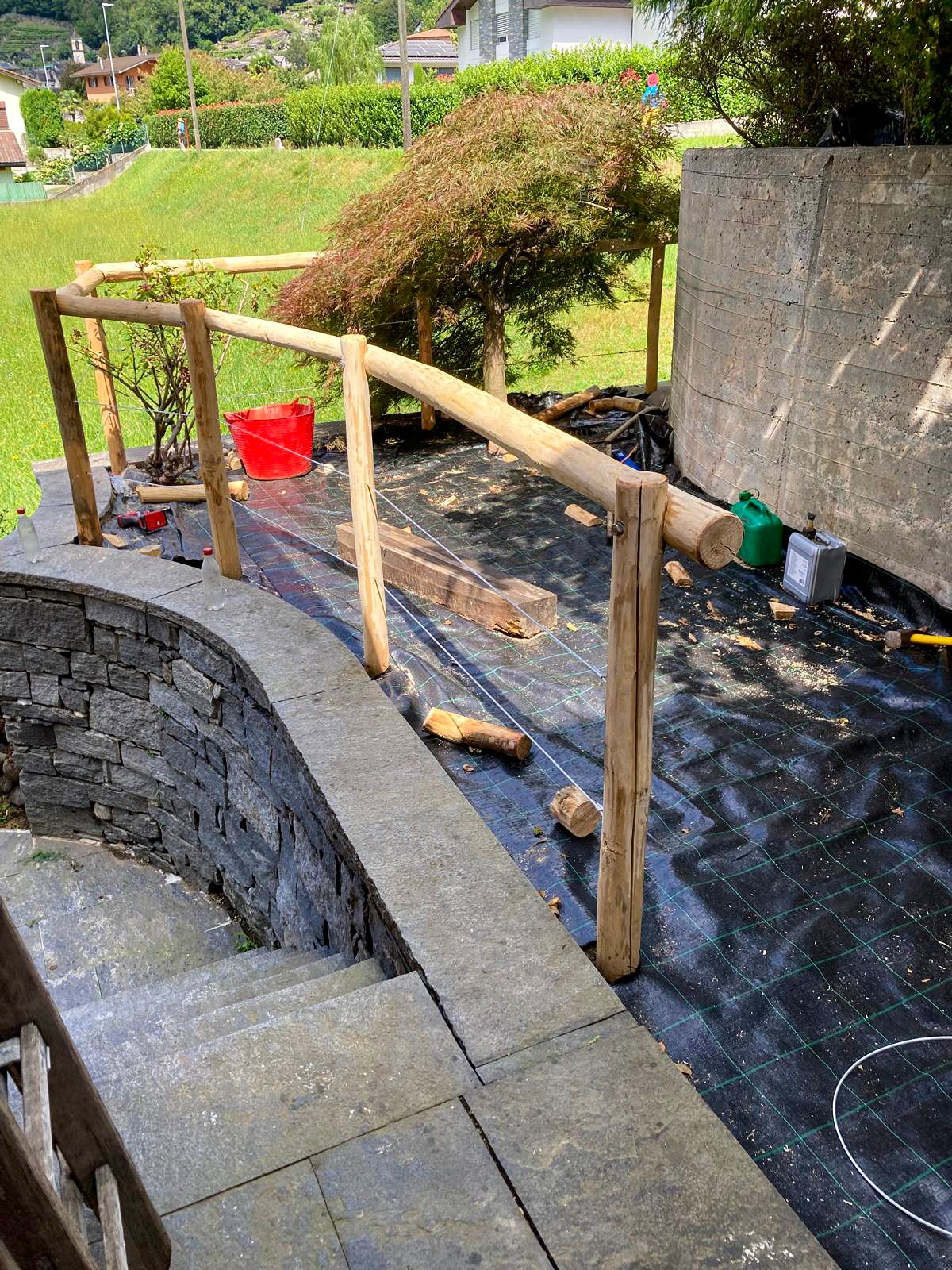 Accanto ad un muro in pietra si sta costruendo una ringhiera in legno.