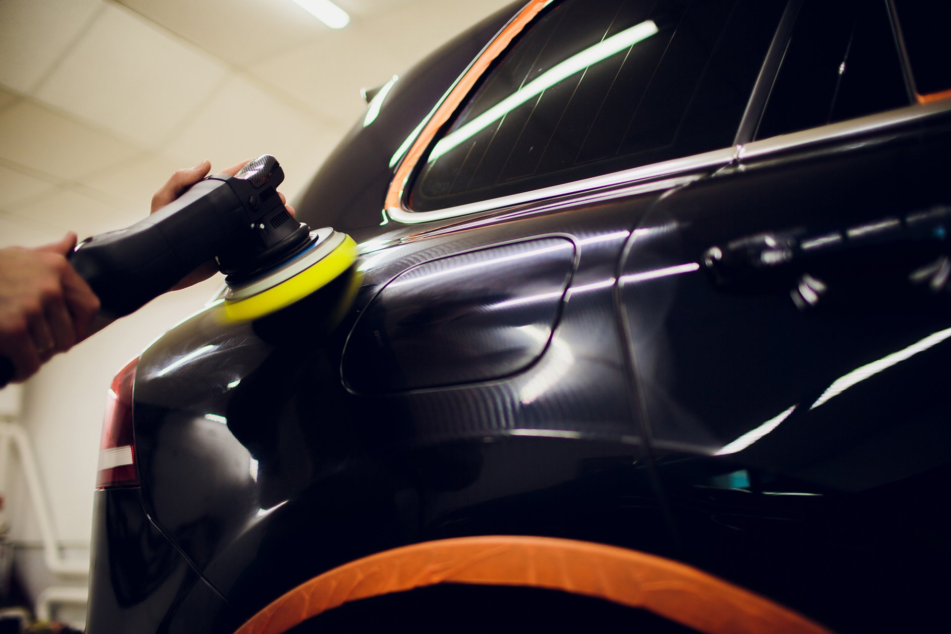 Una persona che lucida un'auto nera con una lucidatrice in un garage.