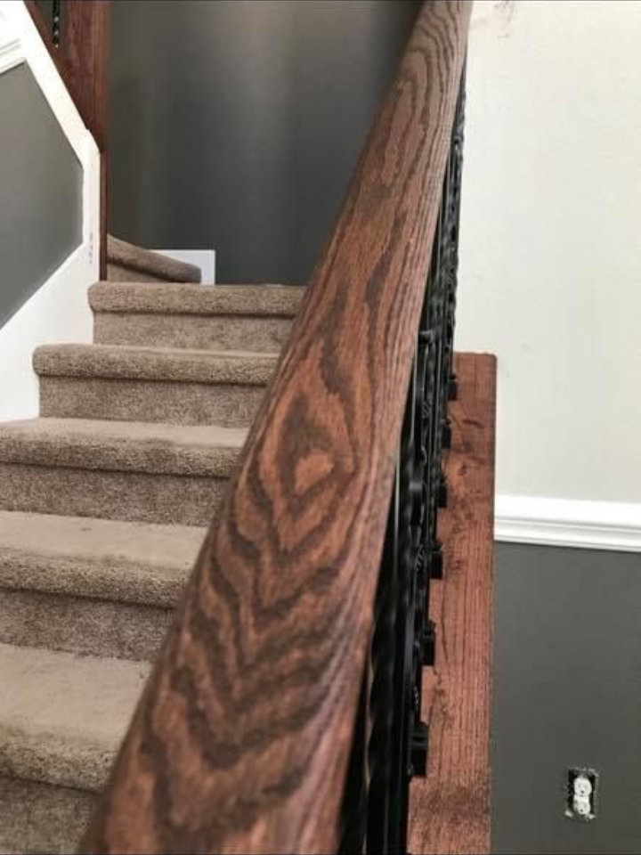 Wooden handrail with decorative dark-colored spindles on carpeted stairs.