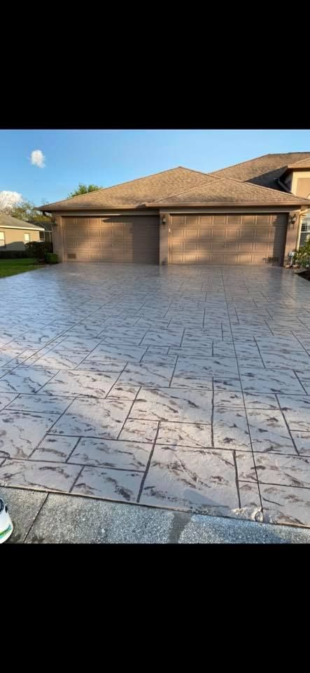 A house with a patterned concrete driveway in front of two garage doors.