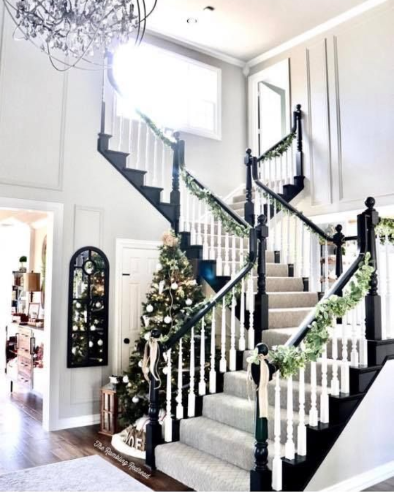 Grand staircase with black railings, white balusters, and festive garland. Decorated Christmas tree.