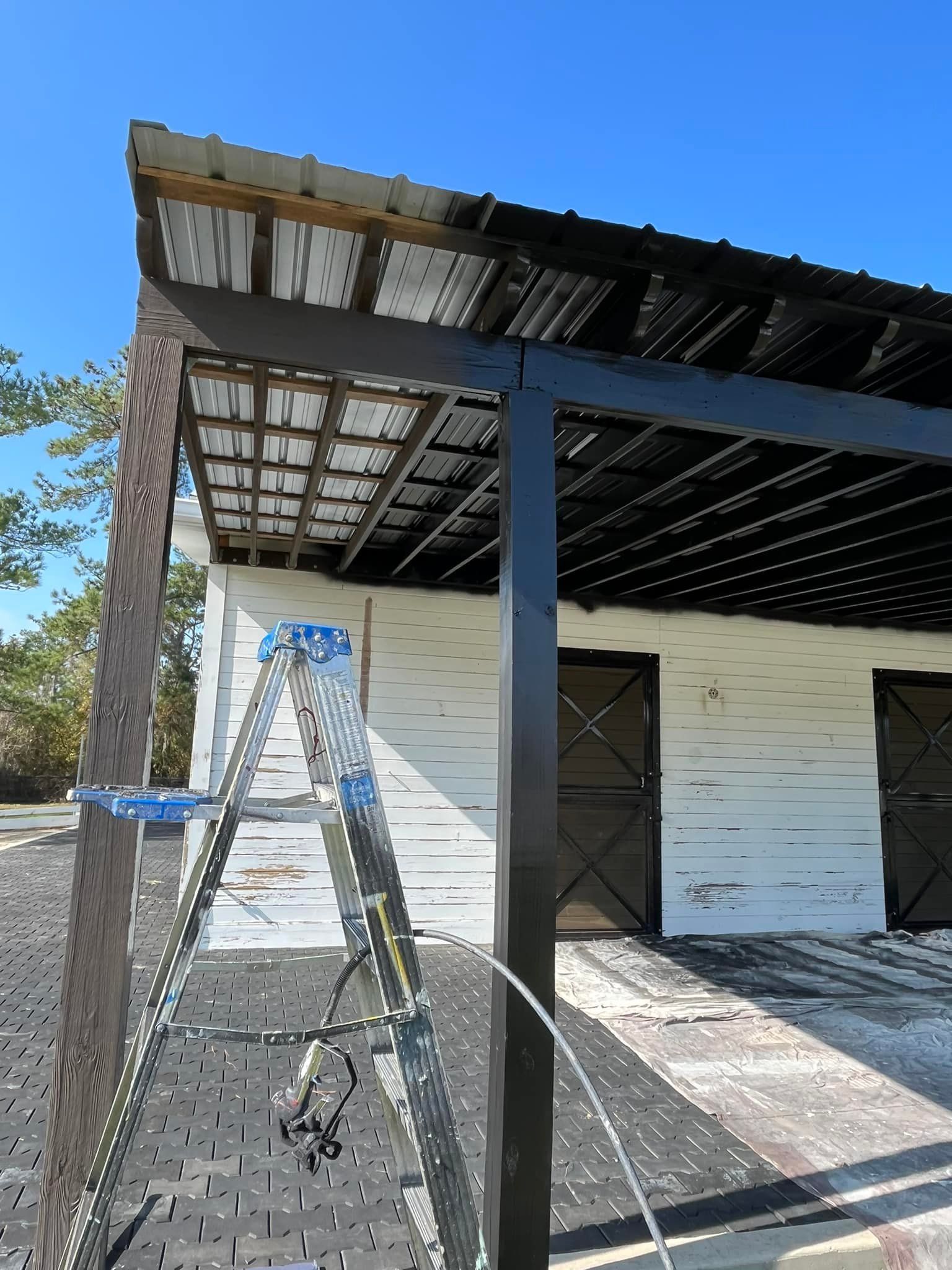 Metal roofed structure being painted black, ladder present.