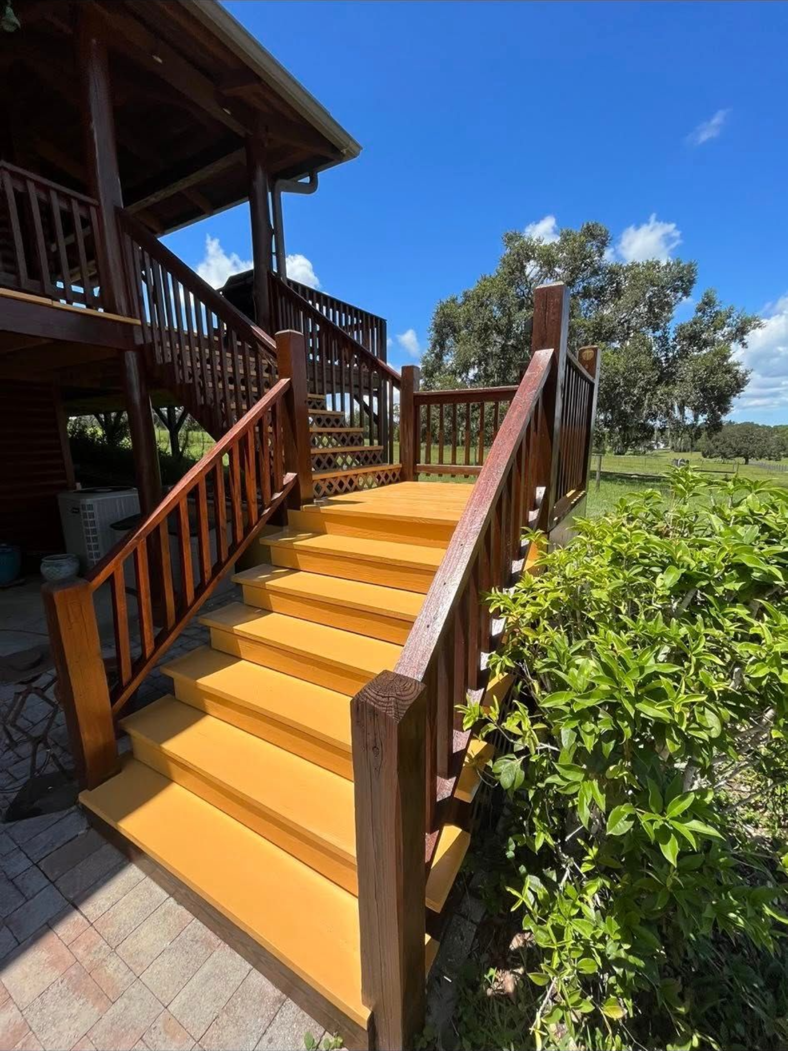 Wooden outdoor staircase with brown railings and yellow steps, leading up to a wooden deck, sunny day.