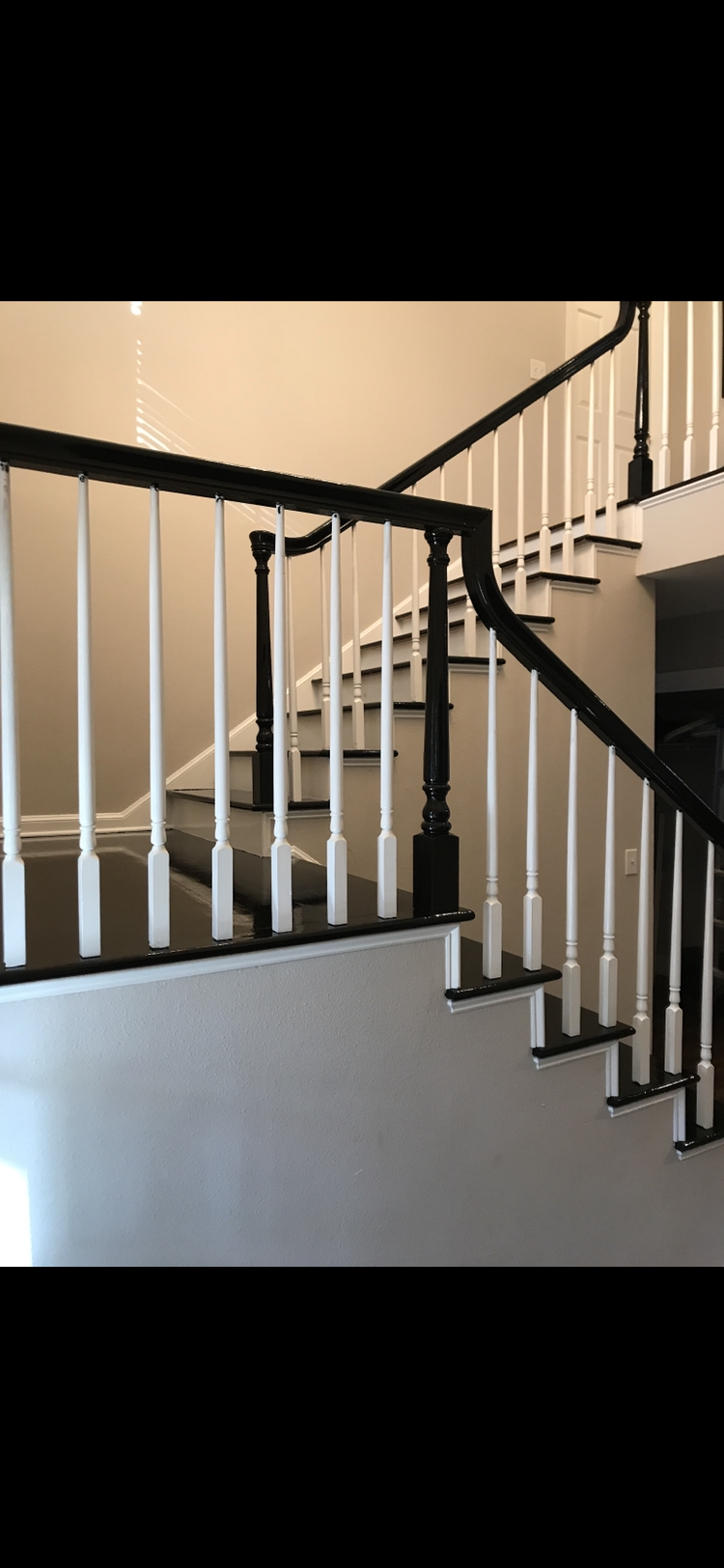 Staircase with white balusters and black handrails and newel posts in a neutral-colored hallway.