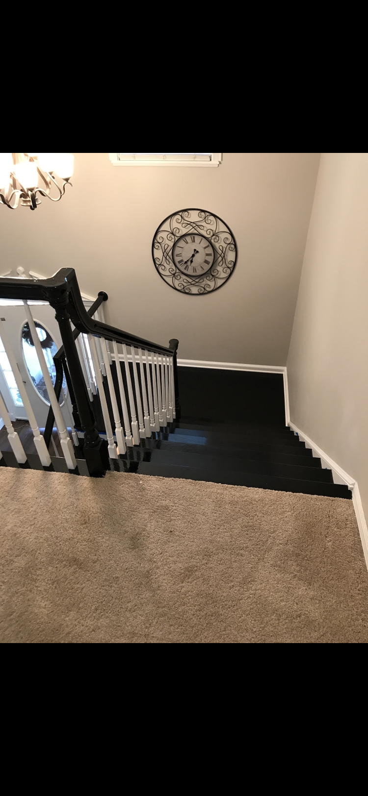 Staircase with black and white railing, tan carpet, and a clock on the wall.