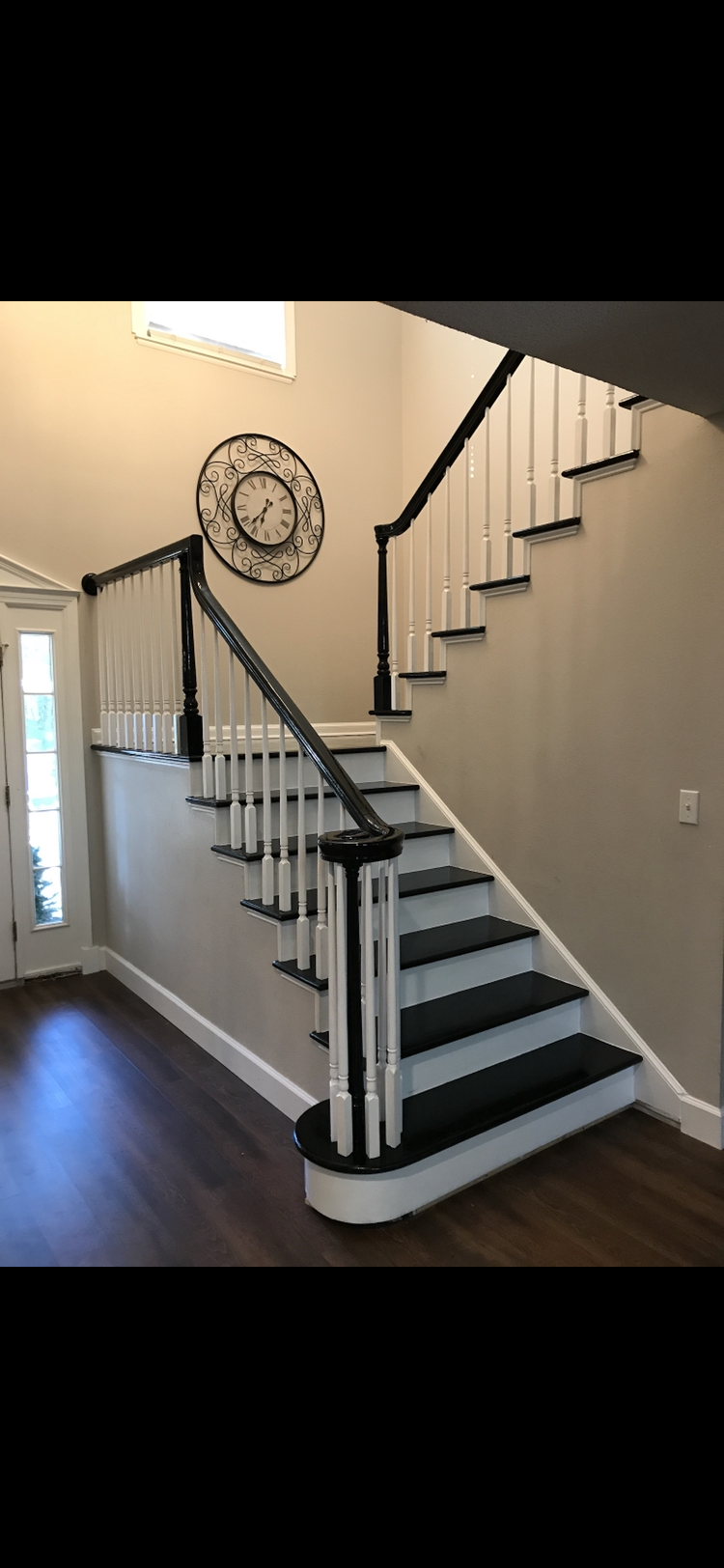 Staircase with black and white accents. Dark wood flooring. Decorative clock on the wall.