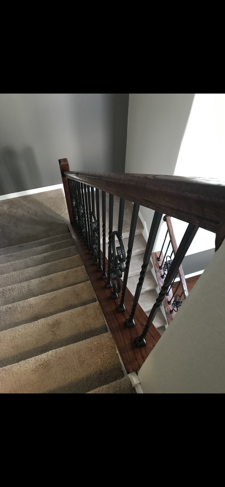 Staircase with carpeted steps and wooden railing with decorative metal spindles.